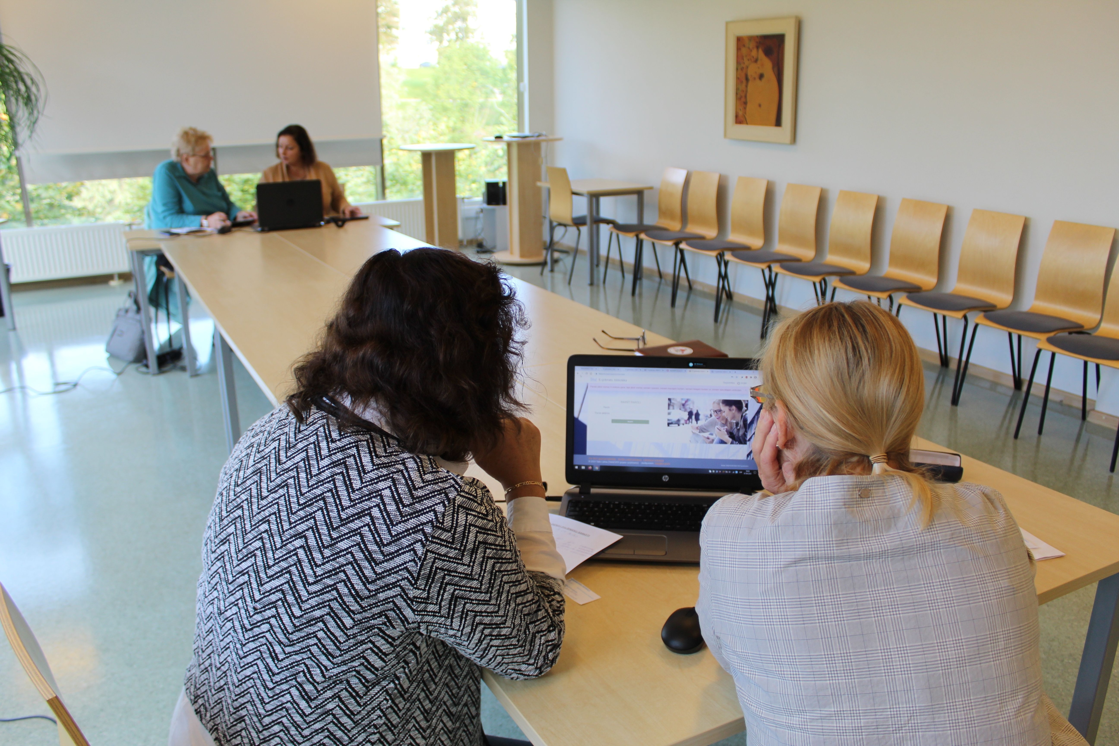 Two groups of people working on laptops in a bright meeting room, during a training or project session.