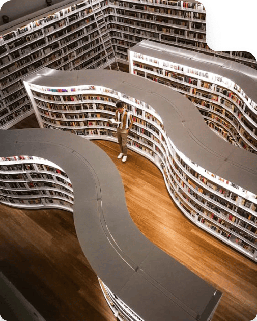 Person standing among curved bookshelves in a modern, well-lit library, viewed from above.